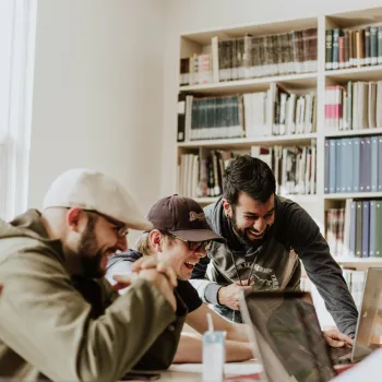 Three men laughing around a laptop computer